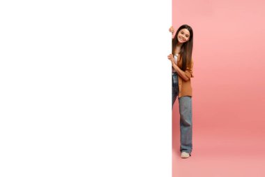 İlginç bir teklif. Beyaz reklam panosunun arkasında, elinde reklam panosu olan, gülümseyen, elinde reklam panosu tutan, kameraya bakan, pembe arka planda duran mutlu genç kız.