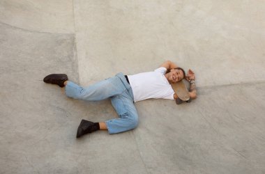 Genç Avrupalı adam kaykay parkındaki rampada dinleniyor ve yatıyor. Enerjik bir kaykay turundan sonra, manzaranın üstünde, serbest alan. Duruşu, şehir ortamında bir memnuniyet ve dinginlik hissi veriyor.