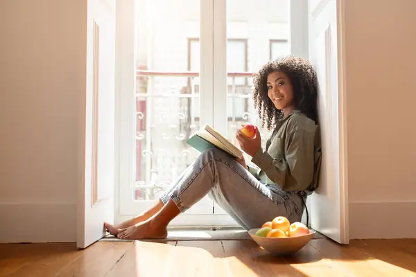 Happy Young Black Woman Reading Book Casa Enquanto Relaxa Piso — Fotografia de Stock