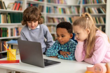 Sınıftaki çeşitli okul çocukları, dikkatle dizüstü bilgisayarda eğitim videoları izliyor, öğrenme yolculuklarını canlı eğitim ortamında artıran dijital kaynakları keşfediyorlar.