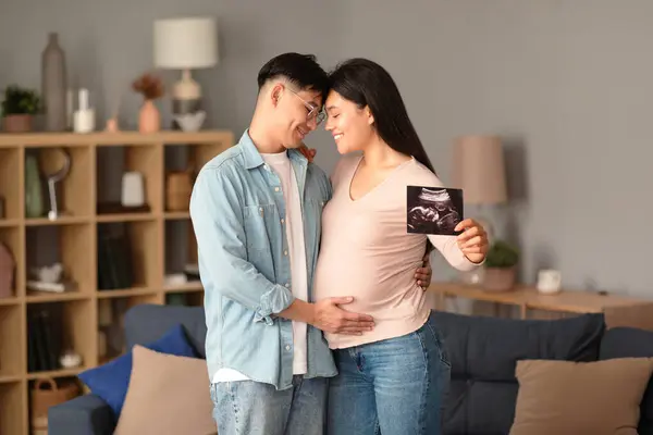 Joyful Asian Spouses Embracing Cozy Living Room Indoors Showcasing Ultrasound — Stock Photo, Image