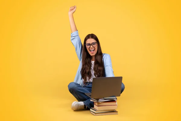 当年轻的女学生在笔记本电脑上体验到胜利或积极的结果 在黄色的工作室背景下被隔离时 她欣喜若狂的一刻 成功的姿态 庆祝学习的胜利 — 图库照片