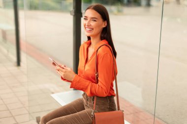 Toplu taşıma. İçerik sahibi yolcumuz cep telefonuyla durakta tramvay bekliyor, tramvay bileti alıyor ve istasyonda otururken internet üzerinden yolculuk ücretini ödüyor.