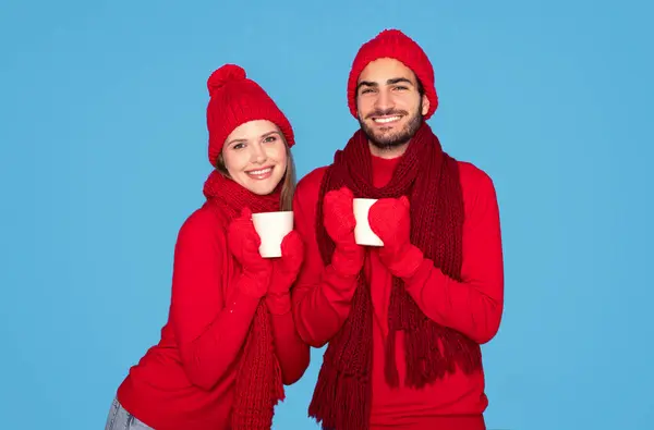 カメラで茶と笑顔のウィンターミットを着ている幸せな若いカップルは 青い背景 コピースペースの上に隔離された暖かい帽子とスカーフで陽気なミレニアルな男と女性 — ストック写真