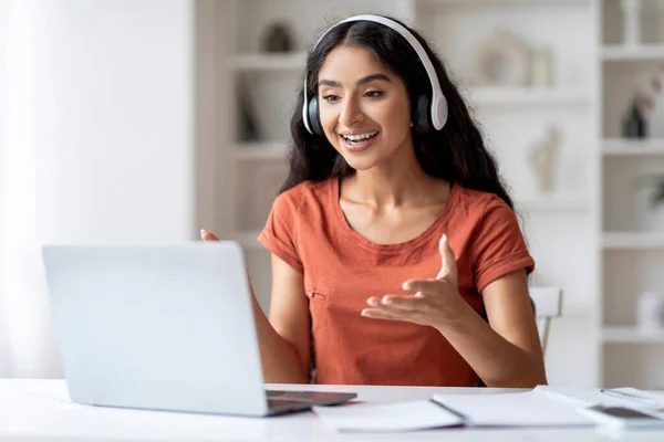 Energetic Freelancer Young Indian Woman Engaging in Virtual Communication. Energetic lady engages in lively, virtual discussions, using laptop and headset, well-organized home office space interior