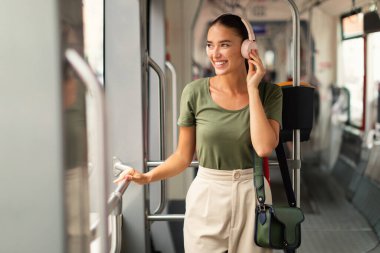 Mutlu kadın internet müziğine dalıyor kulaklık takıyor tramvayda seyahat ediyor, gülümsüyor ve yan bakıyor. Rahat toplu taşıma ve günlük seyahat konsepti