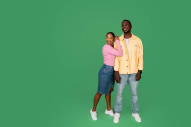 Binlerce yıllık neşeli Afro-Amerikan çifti mesajlaşma ve reklam için fotokopi alanına bakıyor, yeşil renkli stüdyo arka planı, tam boy. İki kişilik teklif, harika bir anlaşma.