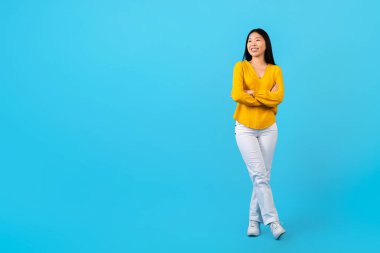 Neşeli, mutlu, çekici, günlük kıyafetler giyen Asyalı bir kadın. Metin ya da reklam için fotokopi odasına bakıyor ve gülümsüyor. Mavi stüdyo arka planında soyutlanıyor.