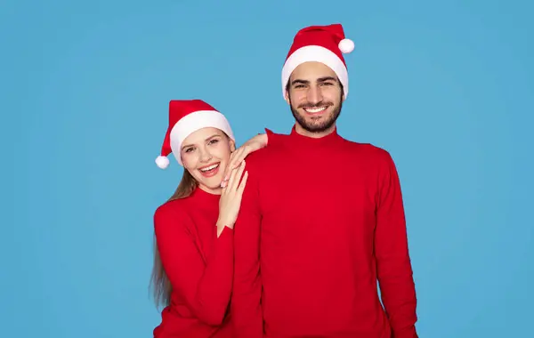 圣诞老人们快乐的年轻夫妇在蓝色工作室背景下的画像 快乐的千禧年男人和女人在相机前拥抱和微笑 共同庆祝圣诞假期 复制空间 — 图库照片