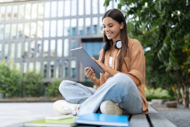 Çevrimiçi alışveriş yapan neşeli genç kız öğrenci dijital tabletini kullanarak, güneşli, canlı üniversite kampüsünde, dijital rahatlığı somutlaştıran, kopyalama alanı. E-ticaret