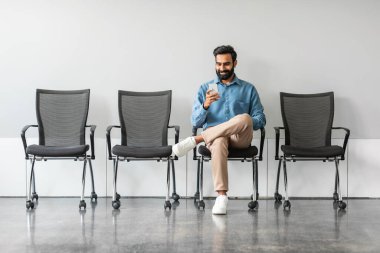 İş adamı, insan kaynaklarıyla görüşmek için bekleme odasında oturuyor. Cep telefonu kullanıyor. İnsan kaynakları, iş kariyeri ve sosyal ağ uzmanı dijital CV 'yi gözden geçirdi