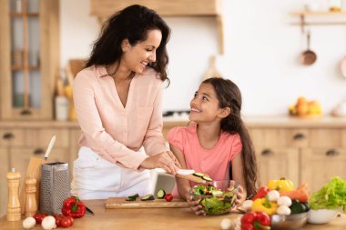 Mutlu anne ve küçük kızı, modern mutfakta birlikte sebze salatası pişiriyor. Sağlıklı yemek pişirme ve sağlıklı yemek hazırlama gibi keyifli anlarda mutlular.