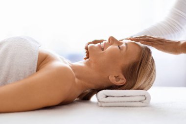 Huzurlu orta yaşlı kadın lüks spa salonunda hafif akapunktur masajı yaptırıyor, profesyonel terapist çekici olgun bir kadınla sağlık tedavisi yapıyor, yan görüş, kopyalama alanı.