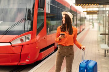 Gülümseyen kadın işe gitmek için cep telefonu kullanıyor ya da havaalanında tramvay durağında bekliyor, seyahat valiziyle duruyor, gelen tren ya da tramvayın yanında poz veriyor, yan bakıyor. Şehir ulaşımı