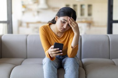 Evde koltukta otururken akıllı telefon ekranına bakan üzgün genç Hintli kadın, depresif Doğu Milenyum Kadın Cep Telefonu Bekliyor, Önemli Arama ya da Sms, Boş Alan