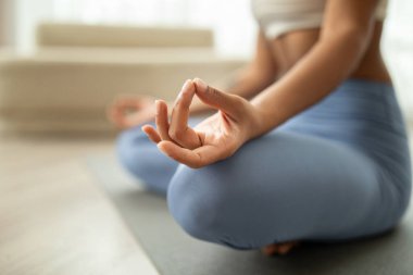 Spor giyimli genç Latin kadın oturma odasının içinde nilüfer pozisyonunda yoga yapıyor. Kapalı, kırpılmış. Evde tek başına eğitim, sağlık hizmetleri, nefes egzersizleri.