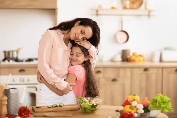 在家里的现代厨房里做蔬菜沙拉的时候 妈妈和女儿都热情地拥抱在一起 在准备晚饭的时候表现出爱心和关心 — 图库照片