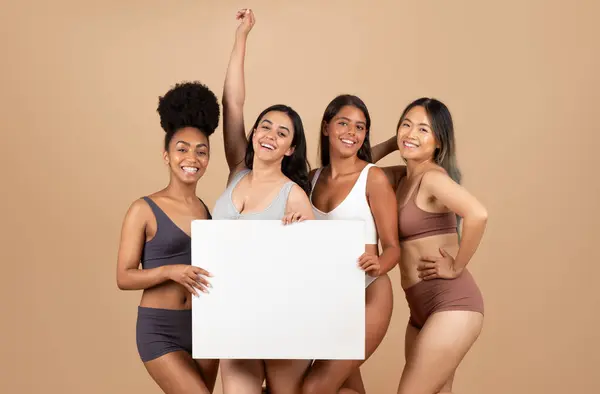 Showcasing beauty and diversity, four multiracial women pose in studio with an empty placard, inviting personalized messages over beige background, mockup