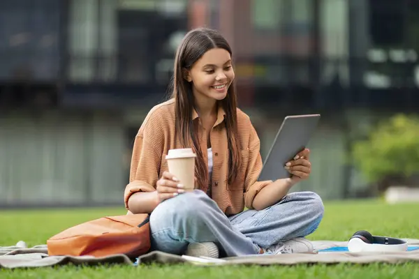 在大学校园的绿色草坪上放松快乐的女学生 休息一下 喝点外卖咖啡 用数码平板电脑 和朋友们一起享受视频电话 通信和小玩意 — 图库照片