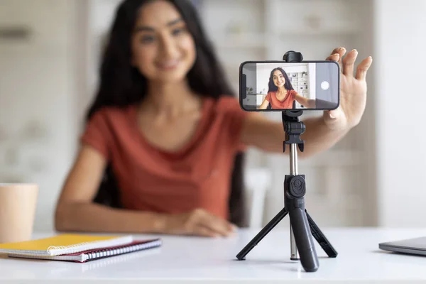 Young hindu woman teacher giving online lesson on smartphone camera, blogger filming video content for social media at home, copy space. Indian lady having educational or business web conference