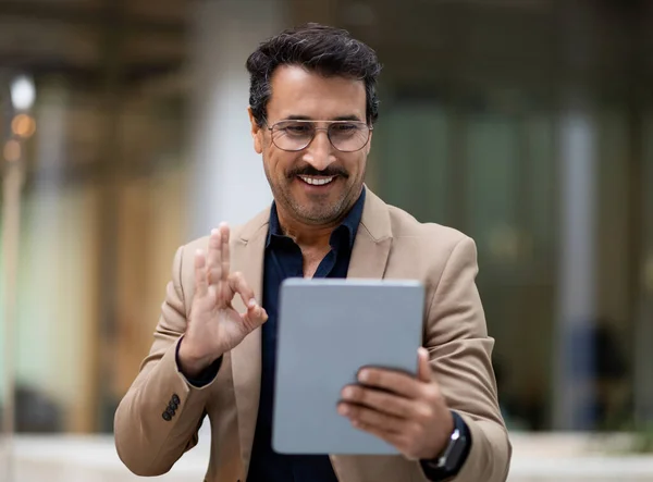 Mature businessman engages in a focused video call using his digital tablet, daily life and technological advancement, showcasing modern communication in urban street, showing okay at screen