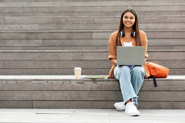精力充沛的女学生一个人坐在空荡荡的大学校园的楼梯上 专心致志地使用笔记本电脑 可能是打电话或参加网上讲座 做作业 抄袭空间 — 图库照片