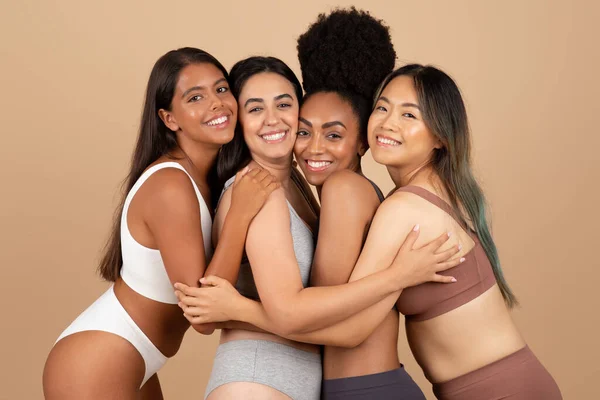 Celebrating beauty in diversity, four ladies of different ethnicities and shapes joyfully pose in their underwear, highlighting an authentic, united front, beige studio background