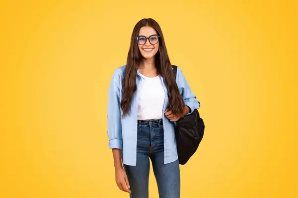 笑聪明漂亮的女学生背着背包 戴眼镜学习 享受在学校学习 隔离在黄色工作室的背景 大学教育 生活方式和课程 — 图库照片