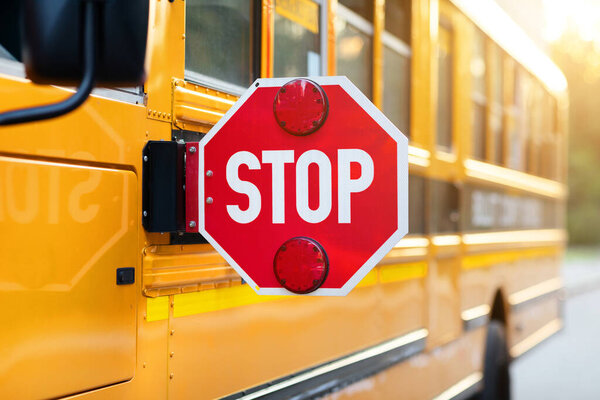 Closeup shot of extended red stop sign on yellow retro school bus, providing secure and protection for children boarding, travel safety and transportation concept, free space