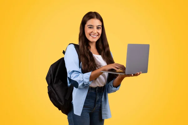笑着带背包的欧洲裔女学生 在笔记本电脑上打字 被黄色背景隔离 生活方式 远程学习和作业 教育和在线课程 视频通话 — 图库照片