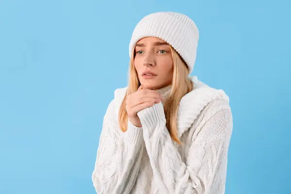 冷たく凍った女性がニットセーターと帽子を被り 青いスタジオの背景に立って手を握る — ストック写真