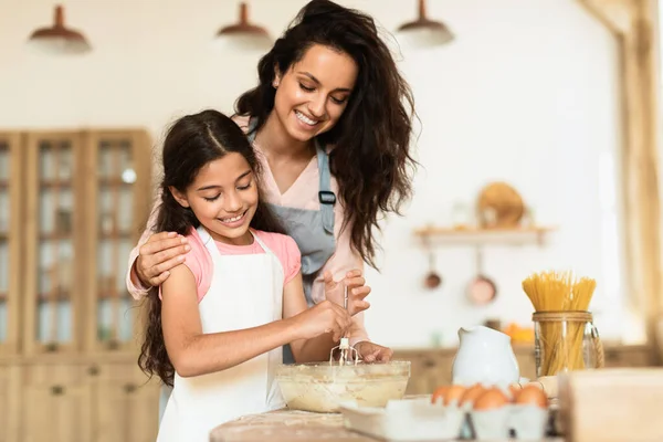 Smiling mother and daughter kneading cookies dough together, engaging in baking session in cozy modern kitchen indoors, embracing joy of pastry preparation and family leisure