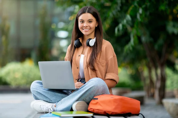 大学校园里一个年轻的女学生用笔记本电脑 脸上带着淡淡的微笑 她的手指轻轻地敲键盘 探索网上内容 做作业 休息时上网 — 图库照片