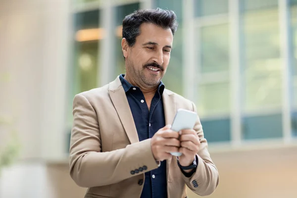 Handsome mature man in formal suit manager using smartphone outdoors. Middle aged businessman chatting on cell phone on the way to business meeting, checking email or business mobile app, copy space