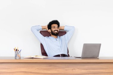 Resmi kıyafet işçisi olan Hintli genç adam, başarılı işini internet üzerinden yürütüyor, kolları başının arkasında bir masada oturuyor, beyaz ofis alanı ile çevrili, çağdaş çalışma ortamı, kopyalama alanı.