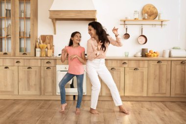 Neşeli genç anne ve kızı mutfakta dans ediyor, eğleniyor ve eğlenceli aile anlarını paylaşıyorlar. Tam yol ileri. Anne ve kız müziğe komik hareketler yapıyor.