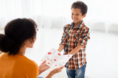 Anneler Günü sürprizi. Neşeli çocuk, tatilde ya da doğum gününde annesini kutluyor, ona el yapımı tebrik kartı veriyor, modern oturma odasında, evdeki iç mekanda kutlama yapıyor.