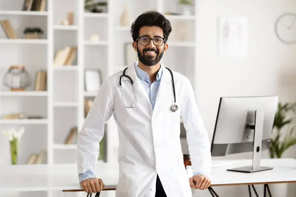 A friendly Indian man healthcare worker, standing at workplace in a clinic, illustrates the convergence of medical practice and digital technology. Modern healthcare concept, copy space