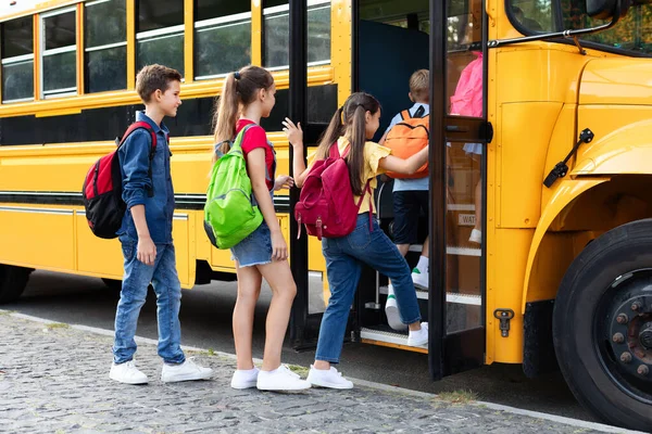Group of happy excited children boarding yellow school bus, diverse kids with backpacks getting in schoolbus, boys and girls going home together after lessons, climbing stairs of vehicle