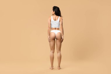 Vücut Bakımı. Stüdyoda bej arka planda duran zayıf, spor iç çamaşırlı kadın, mükemmel atletik iç çamaşırı giyen güzel genç kadın, fotokopi alanı ile tam uzunluk