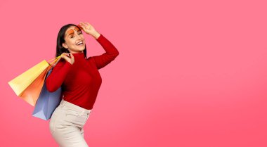 Parlak alışveriş torbaları olan, güneş gözlüğünü çıkaran, kameraya bakan, gülümseyen, büyük satışlardan zevk alan, pembe arka planda duran, uzay kopyası olan güzel, mutlu bir kadın.