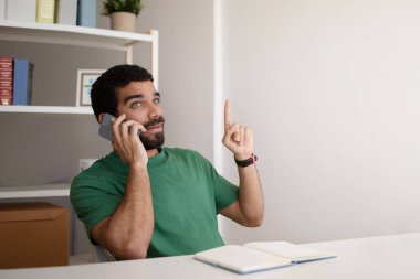 Milenyum Arap menajeri telefonda müşteriyle konuşuyor, ev içi ofis içi boşluğu işaret ediyor. İş ve iletişim, fikir işareti var.