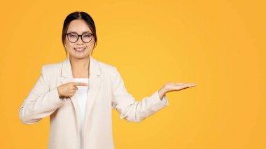 Gülümseyen bin yıllık Koreli kadın elinde fotokopi aletiyle parmakla işaret ediyor, sarı stüdyo arka planında izole edilmiş, panorama. İş tavsiyesi, satış ilgisi, insanların duyguları, reklam ve sunum