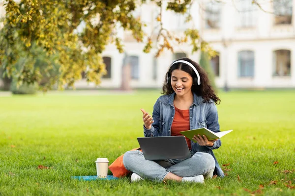 Young Eastern Woman Study Outdoors With Laptop And Headphone, Smiling Indian Lady Student Preparing For Exam Outside, Sitting On Lawn In Park, Enjoying Online Education, Copy Space