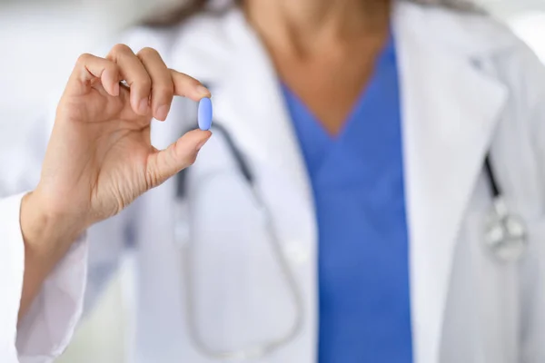 Cropped of woman doctor holds one medical pill in her hand close-up. Unrecognizable doc reminds about correct dose for taking medicine. Drugs, medication, vitamins and supplements