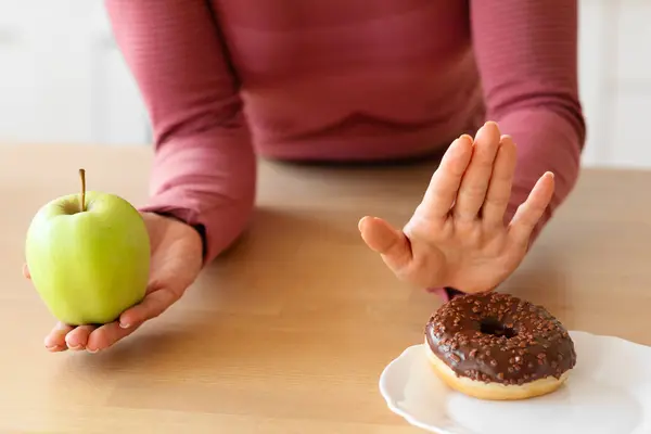 ドーナツの上に緑のりんごを選ぶ認識できないフィットネス女性のクローズアップ キッチンで不健康なデザートへのジェスチャー停止 クロップショット 健康的な食べ物を選択し 果物を食べる女性 — ストック写真