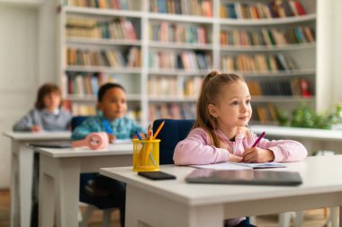 Sınıfta sıralarında oturan bir grup özenli ve çeşitli okul çocuğu, dikkatle öğretmenlerine odaklanıyorlar, bilgiyi özümsüyorlar ve ders sırasında saygılı bir şekilde dinliyorlar.