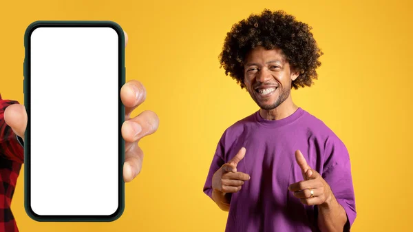 微笑着的非洲裔美国年轻人用手指对着相机 用屏幕空白的智能手机近距离挑选你 隔离在黄色的工作室背景下 App Recommendation Turn Website — 图库照片
