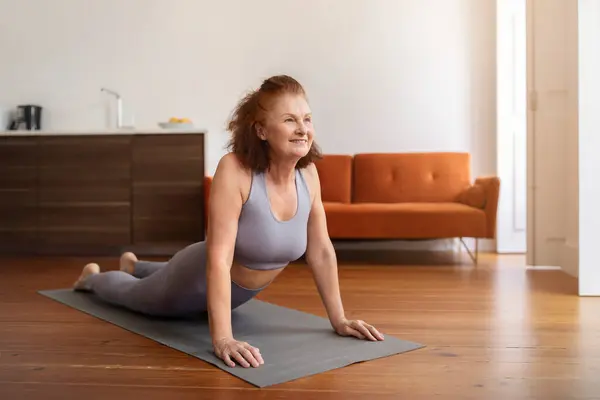 Smiling Senior Woman Training At Home, Making Cobra Pose Exercise, Active Older Lady Exercising On Yoga Mat In Living Room Interior, Sporty Elderly Female Enjoying Domestic Workouts, Copy Space