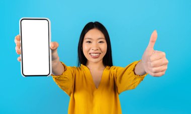 Güzel mobil uygulama, güzel online teklif, anlaştık. Mutlu, genç, güzel Çinli bir kadın beyaz ekranlı ve başparmağı yukarıda, mavi arka plan, kopya alanı, maket, panorama